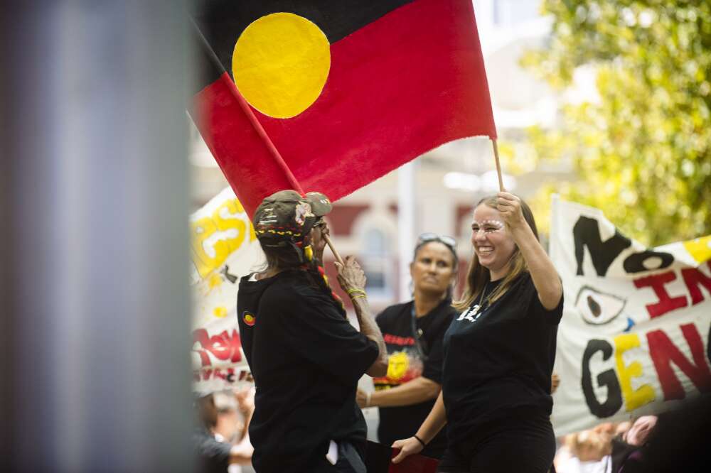 Two First Nations women smiling holding a large Aboriginal flag