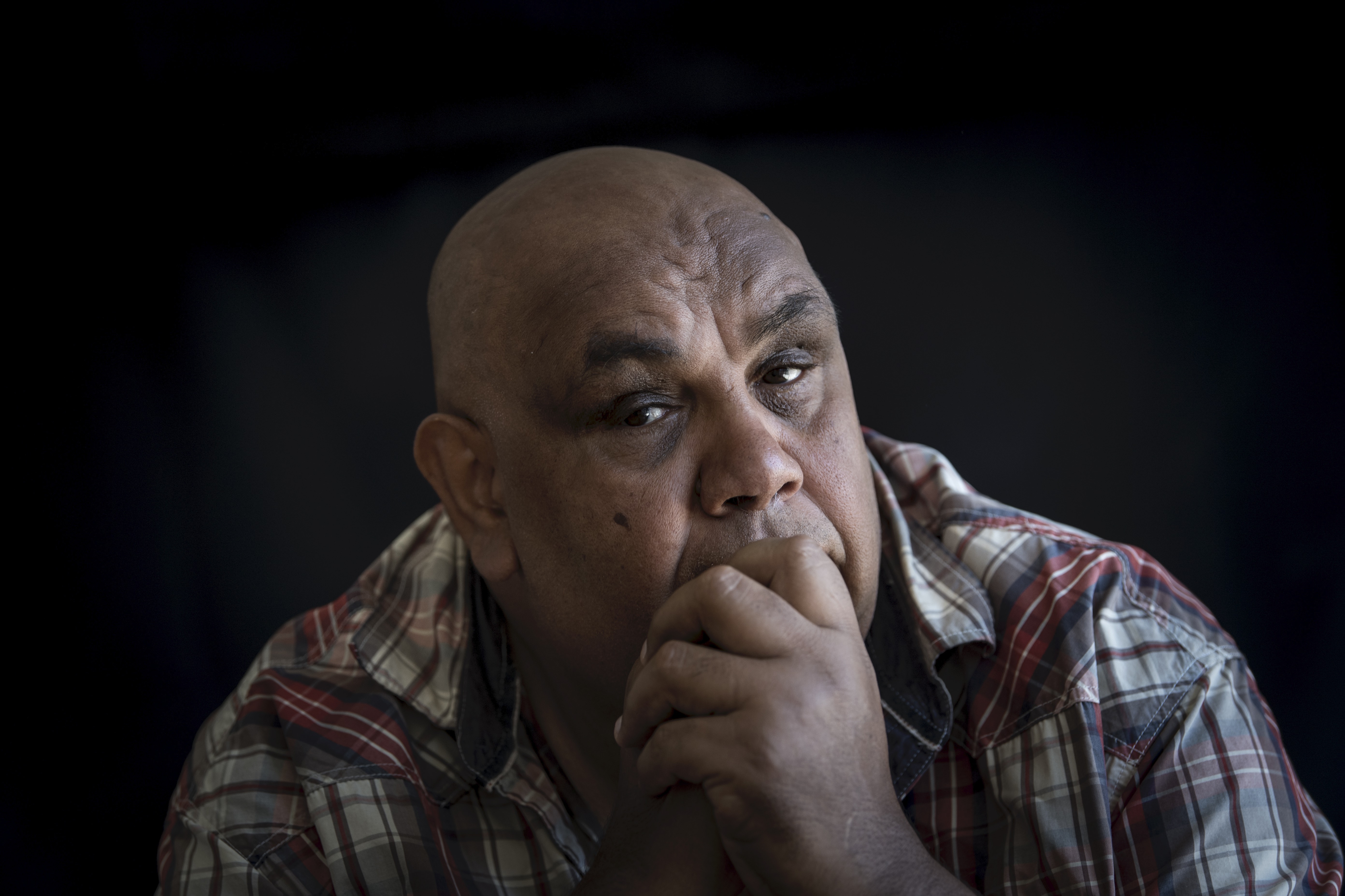 A color portrait of Kutcha Edwards, pensive, with his hand resting on his chin, looking directly at the camera.