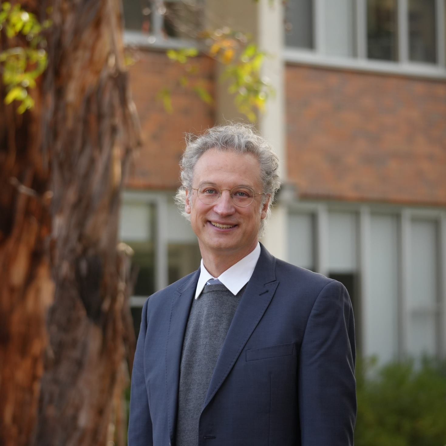 Professor Chris Danta wearing a blue suit and tie, standing in front of a building