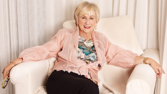 Woman, Libby Hathorn, smiling and sitting on a white armchair with her arms out