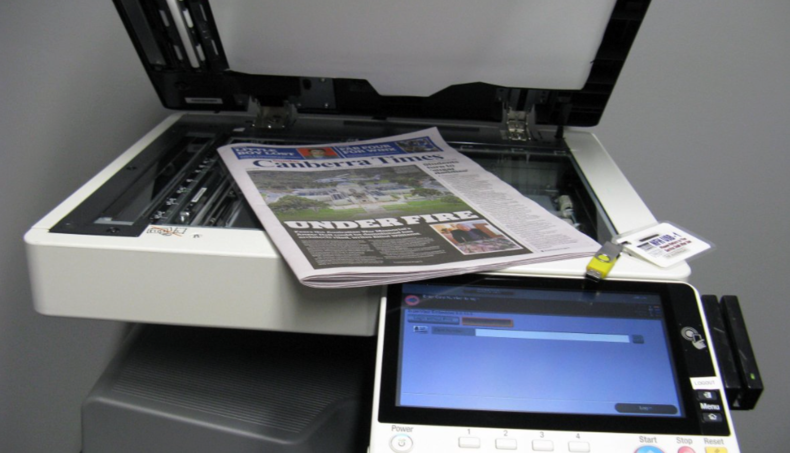 A multi-function device (print, photocopy, scan) with its top open and a newspaper placed on the glass