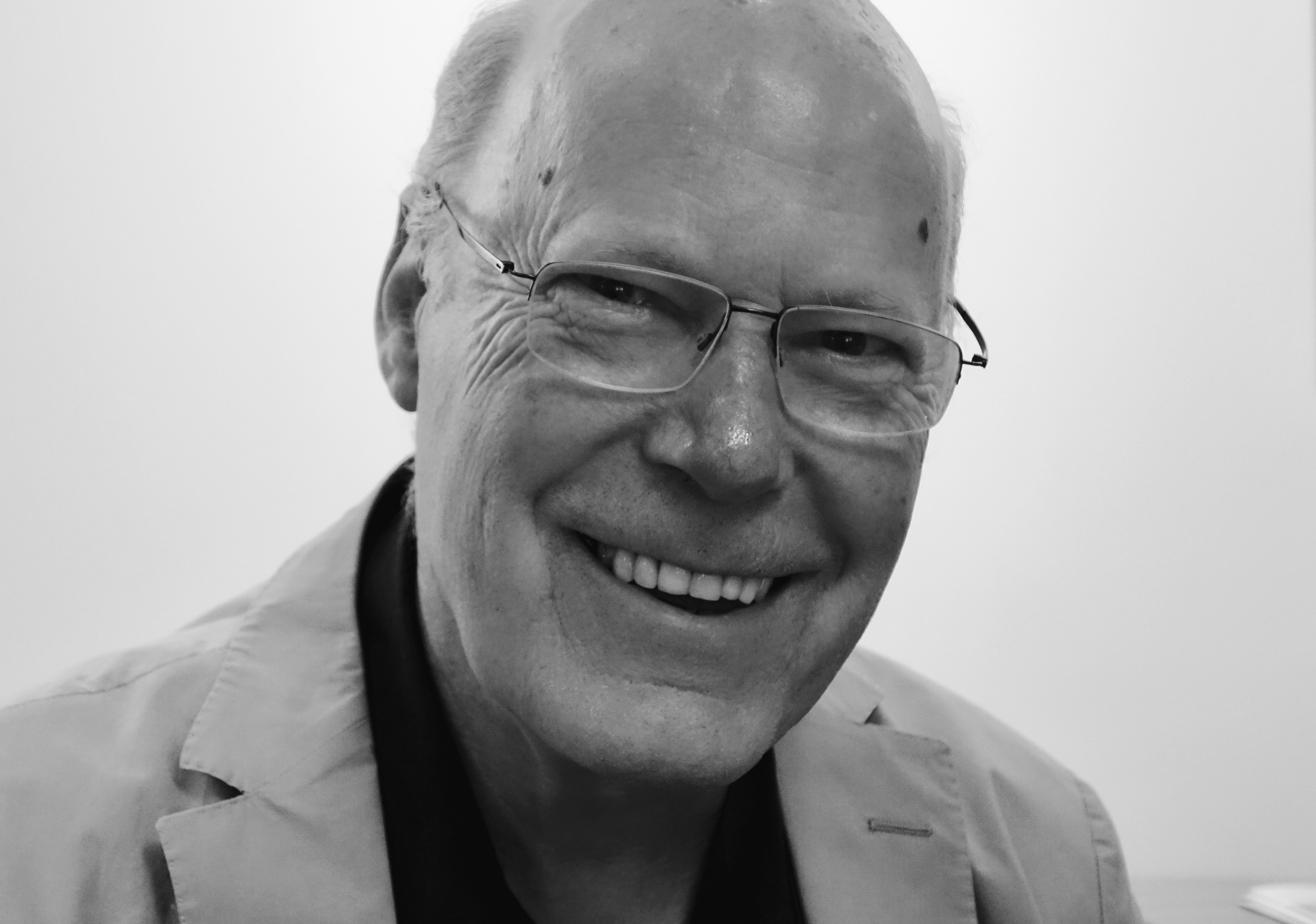 A close up black and white image of man wearing a jacket and glasses