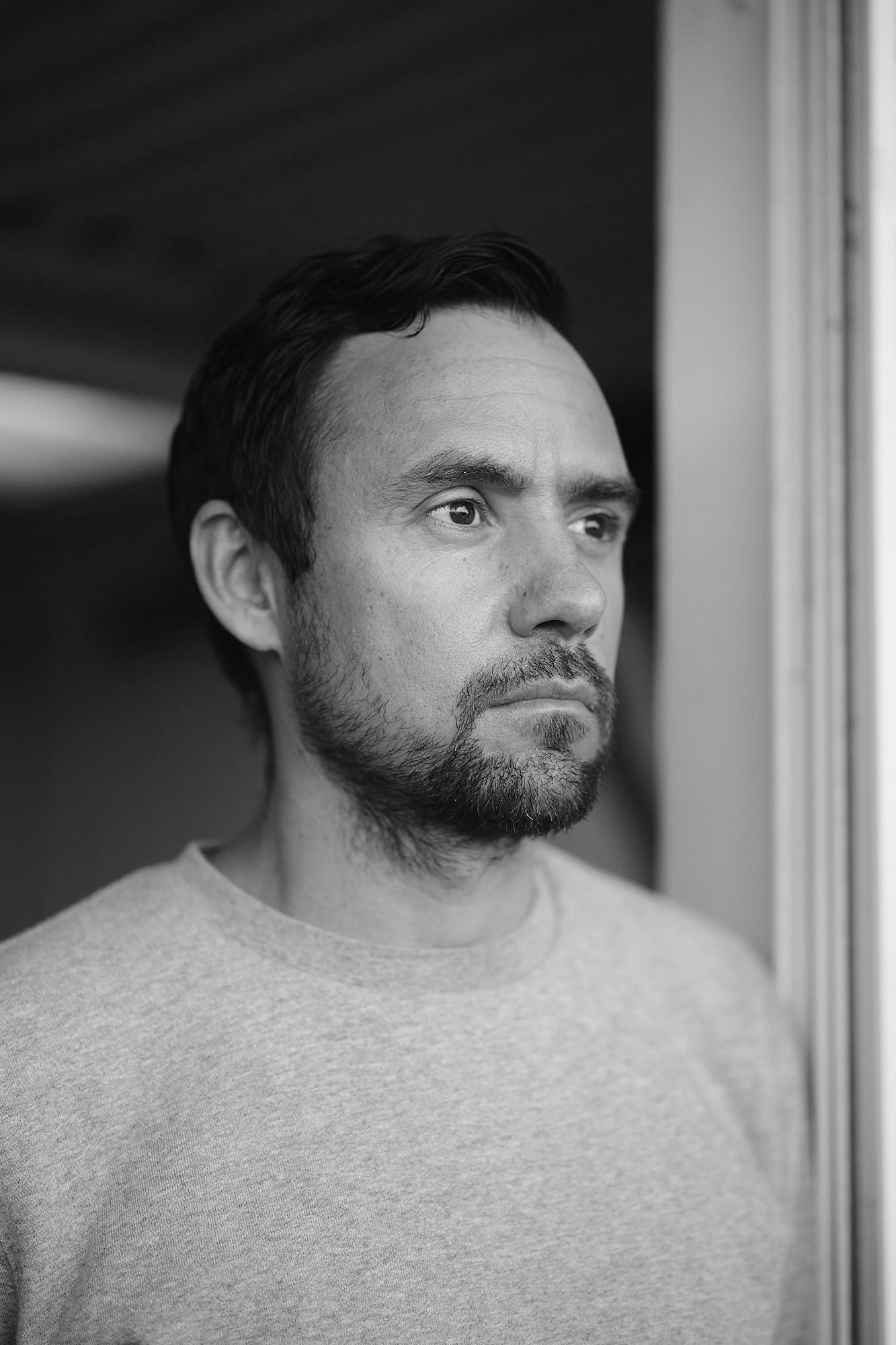 A black and white close up image of a bearded man with short dark hair