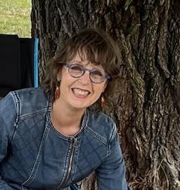 A woman with short, brown hair and glasses wearing a denim jacket
