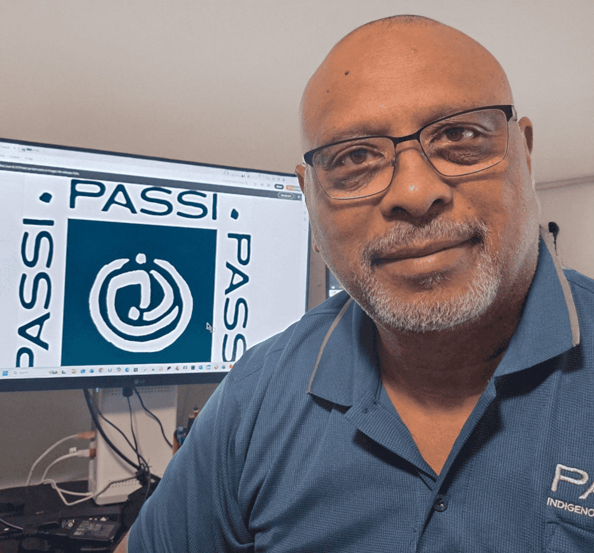 Michael Passi in a blue polo shirt, with a computer screen behind him to his left with the Passi Logo