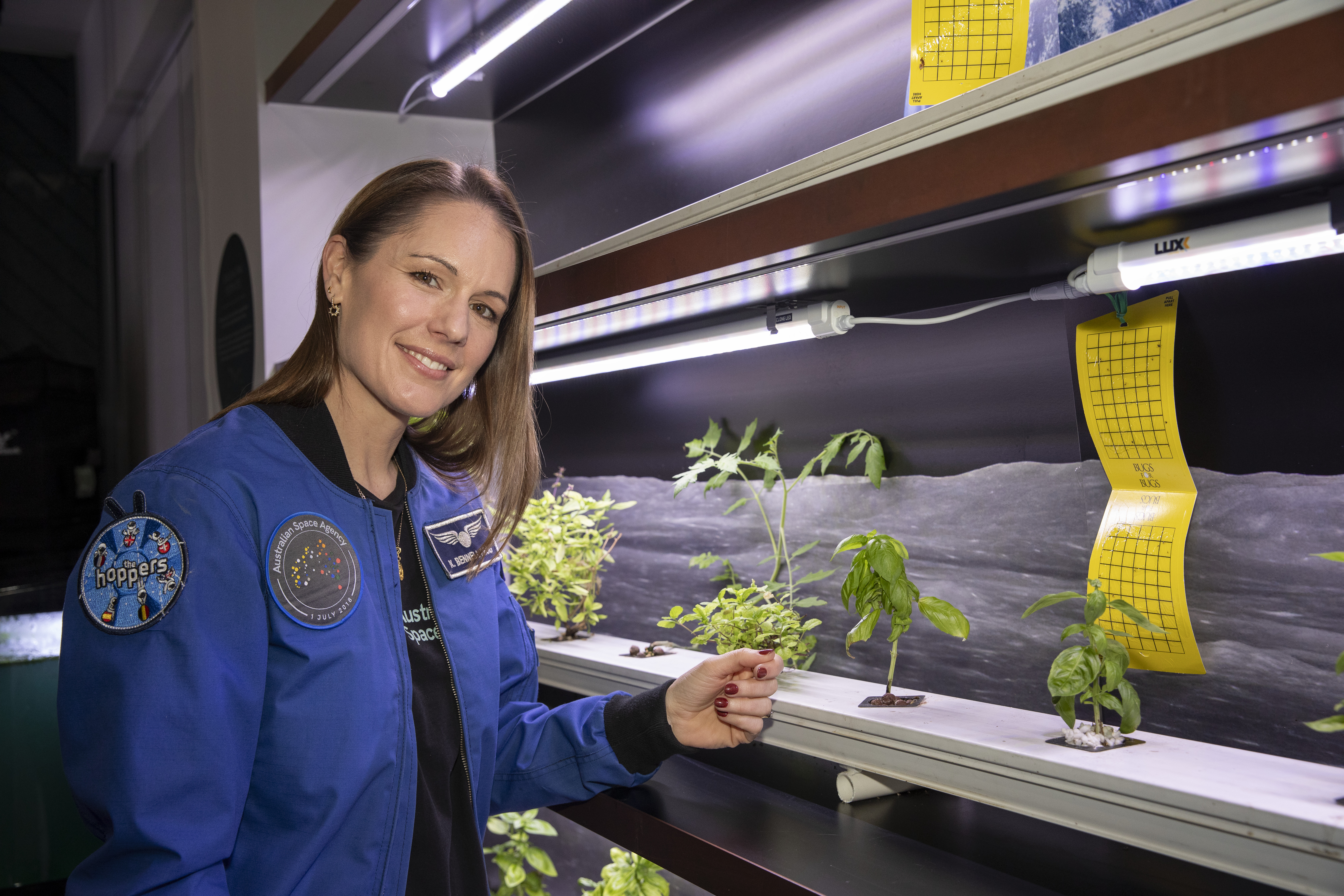 Portrait of Katherine Bennell-Pegg as she stands next to a shelf of plants under grow lights