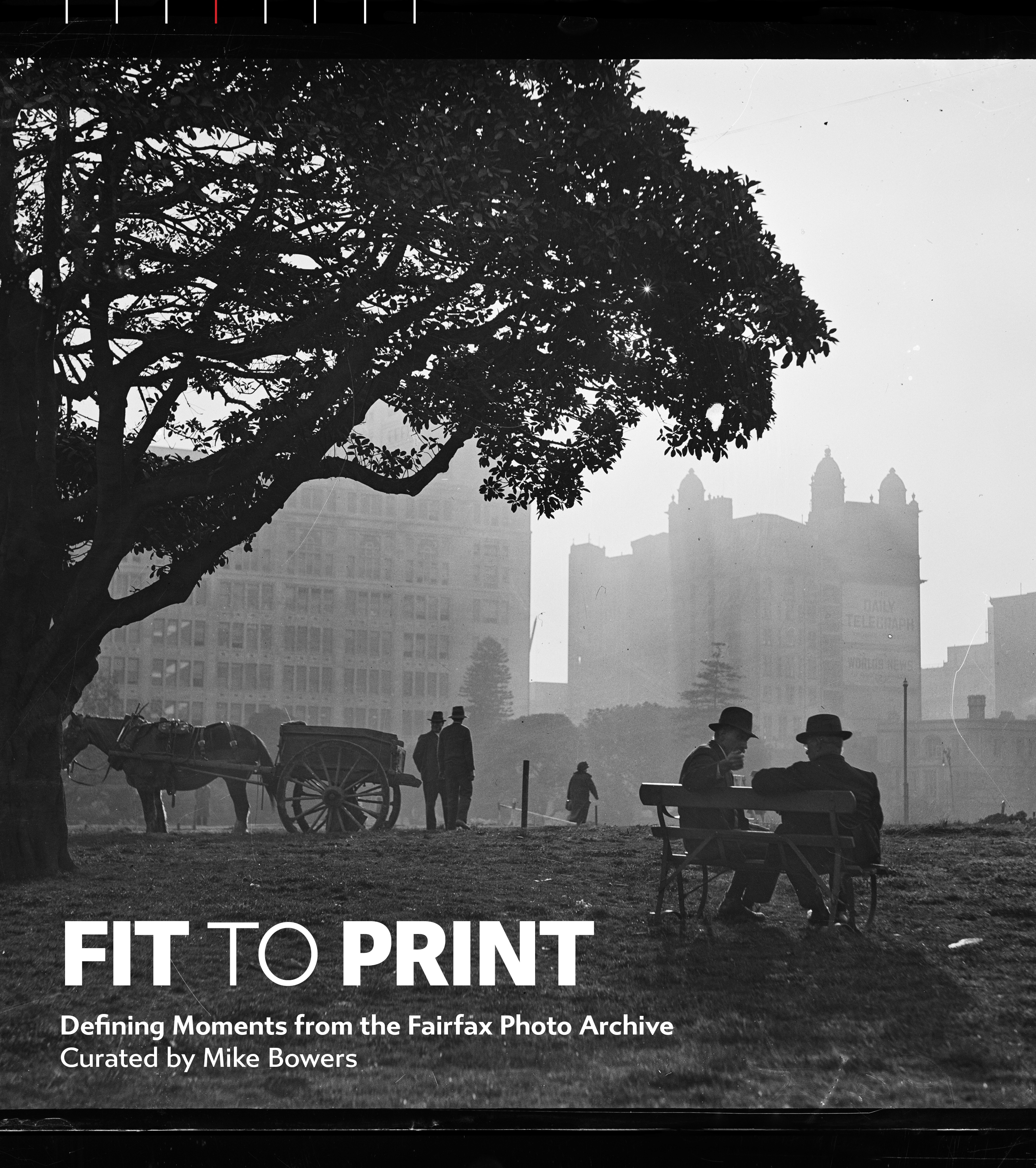 A vintage black and white photograph featuring a large, dark tree dominating the left side, casting shadows over a street scene with an old horse-drawn carriage and several figures. In the background, there are large, imposing buildings, possibly from a city or fairground setting. The image is presented with a 'FIT TO PRINT' overlay.