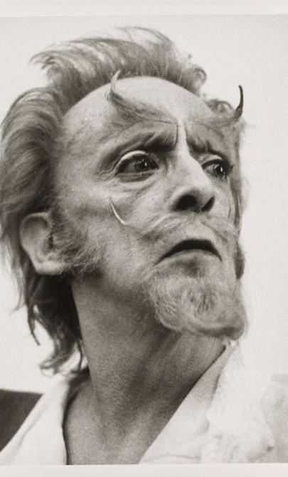 A man with beard, moustache and long eyebrows looks over his left shoulder.