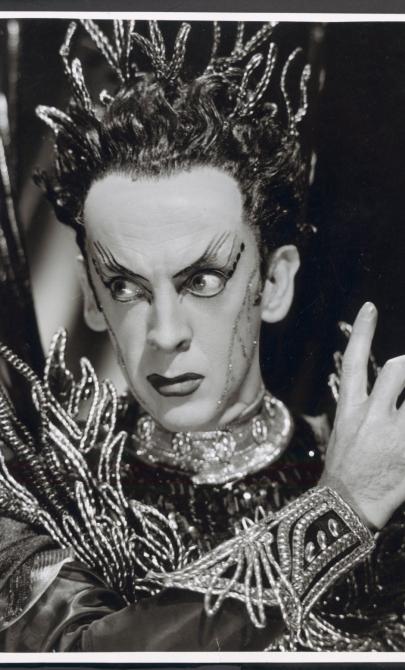 Black and white closeup photograph of Robert Helpmann in stage makeup, wearing a costume that features a beaded headpiece, cuff and collar.