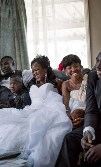 A family dressed for a wedding laughs as they sit together on a couch