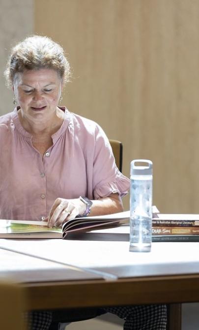 Woman in pink blouse sitting at a table in the Library's main reading room looking through a book