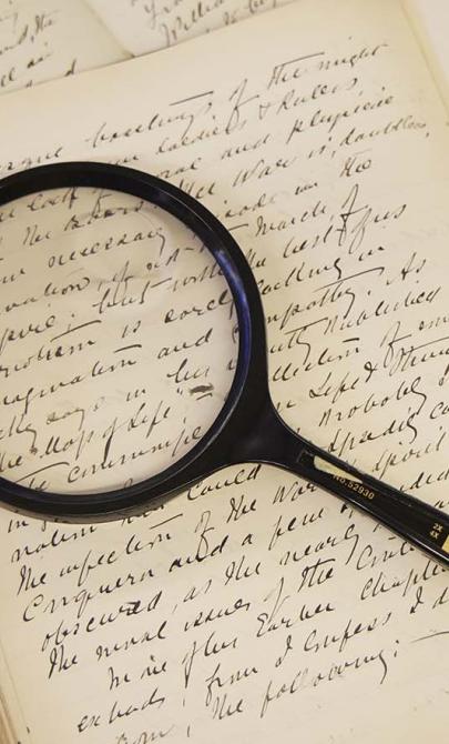 A magnifying glass sits on an old book with handwriting in it