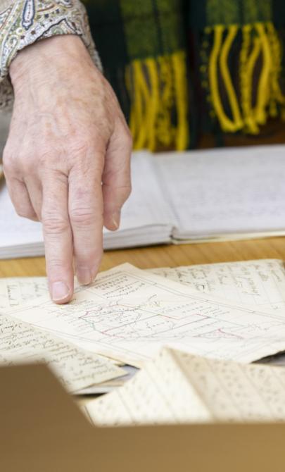 Woman's hand pointing at something on a map on a table with various manuscript material
