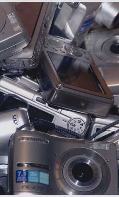A pile of digital cameras sit on a table
