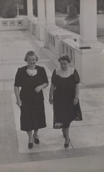 Black and white photo of two women, Dorothy Tangney and Enid Lyons, walking together towards the entrance of Old Parliament House 