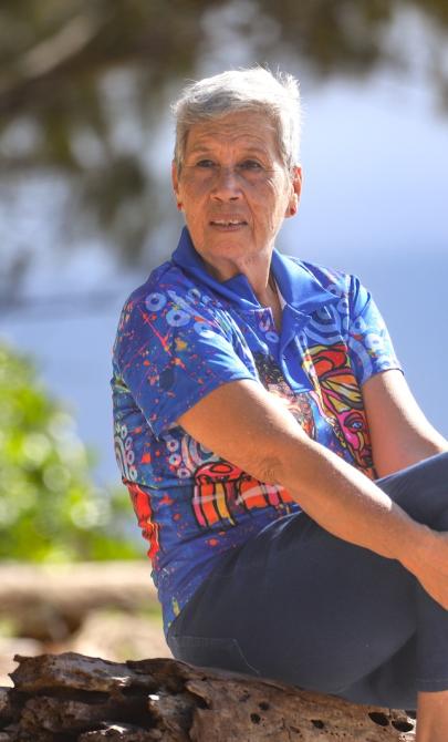 Fijian Australian woman with short grey hair sitting on a rock on a beach