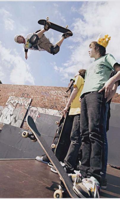 A man in the air doing a trick on a skateboard on the left with some young men watching him on the right