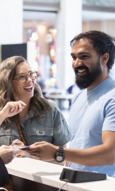 Man and woman smiling as they are being greeted and having questions answered at the front information desk in the Library foyer