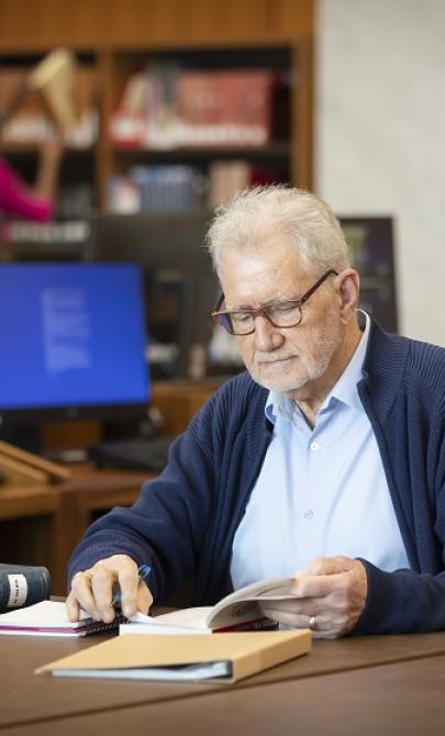 Man sitting at a table in the Main Reading Room reading a book with a notebook and pen nearby