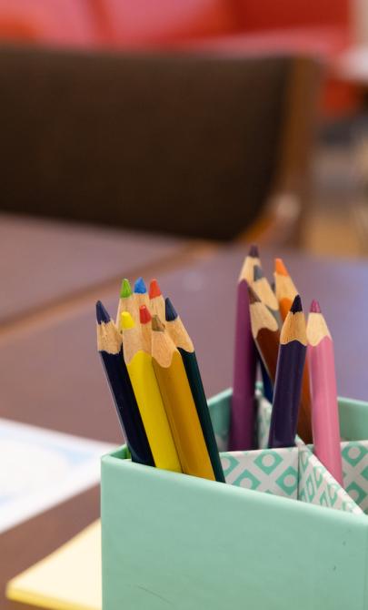 Cup of coloured pencils on a table with colourful worksheets nearby