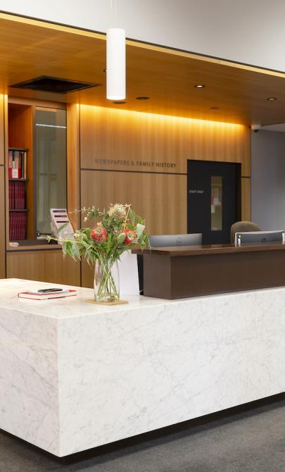 Librarian wheeling a trolley with collection material around the Newspapers & Family History Zone desk