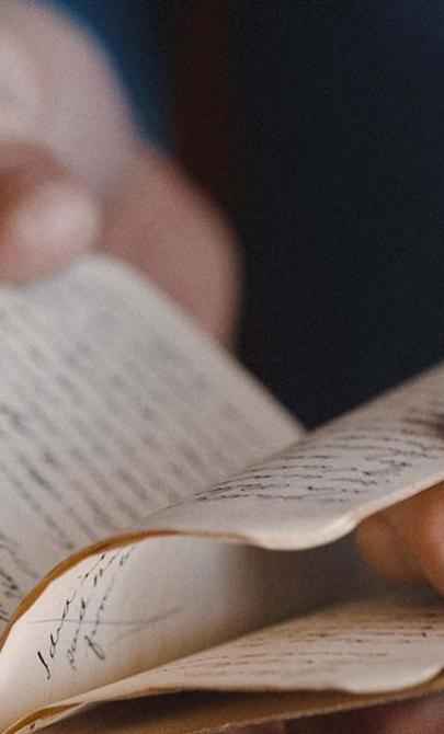 Close-up of a person's hands carefully turning the pages of an old, handwritten journal.