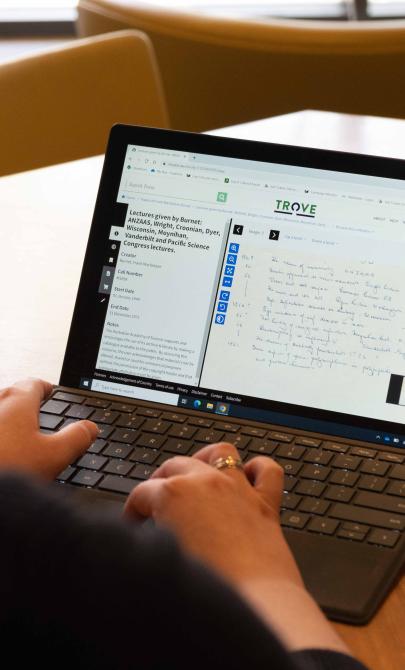 Over the shoulder of woman using laptop. On her screen she is using Trove to look at digitised handwritten notes from a lecture