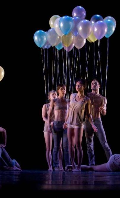 Dancers standing, crouching, and laying down holding balloons