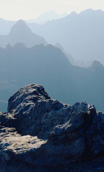 A sweeping landscape of a mountain range. The mountains are craggy and rocky. They are covered in mist.
