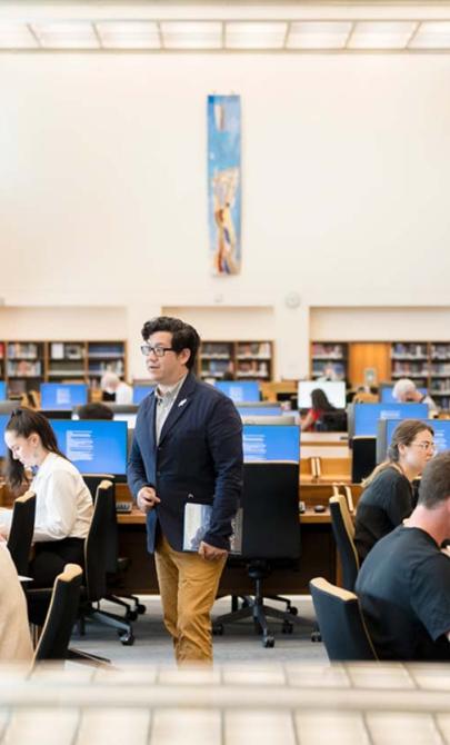 A man talks to a woman in the reading room of the National Library of Australia while other people work at tables and computers