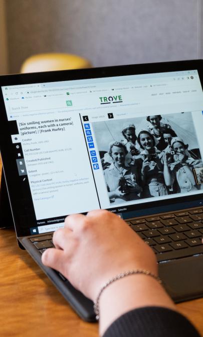 Over the shoulder of woman using laptop. On her screen she is using Trove to look at a digitised photo of nurses