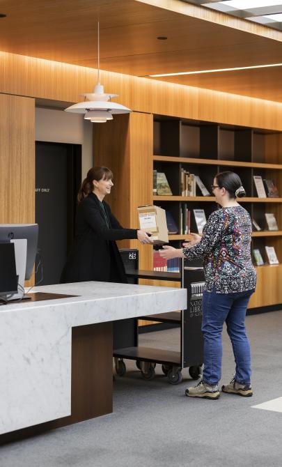 Library staff member handing a box of collection material to a woman in the Special Collections Reading Room