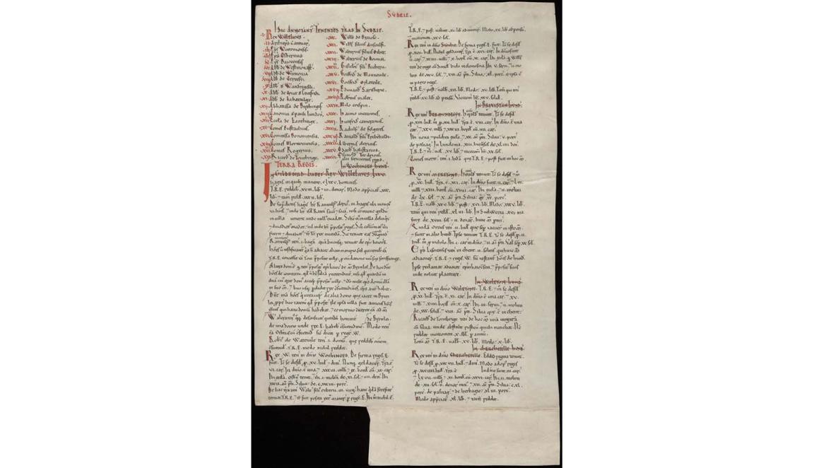 A facsimile copy of the Domesday Book. It is missing a square from the bottom left hand corner. Some of the text is black and some is red.