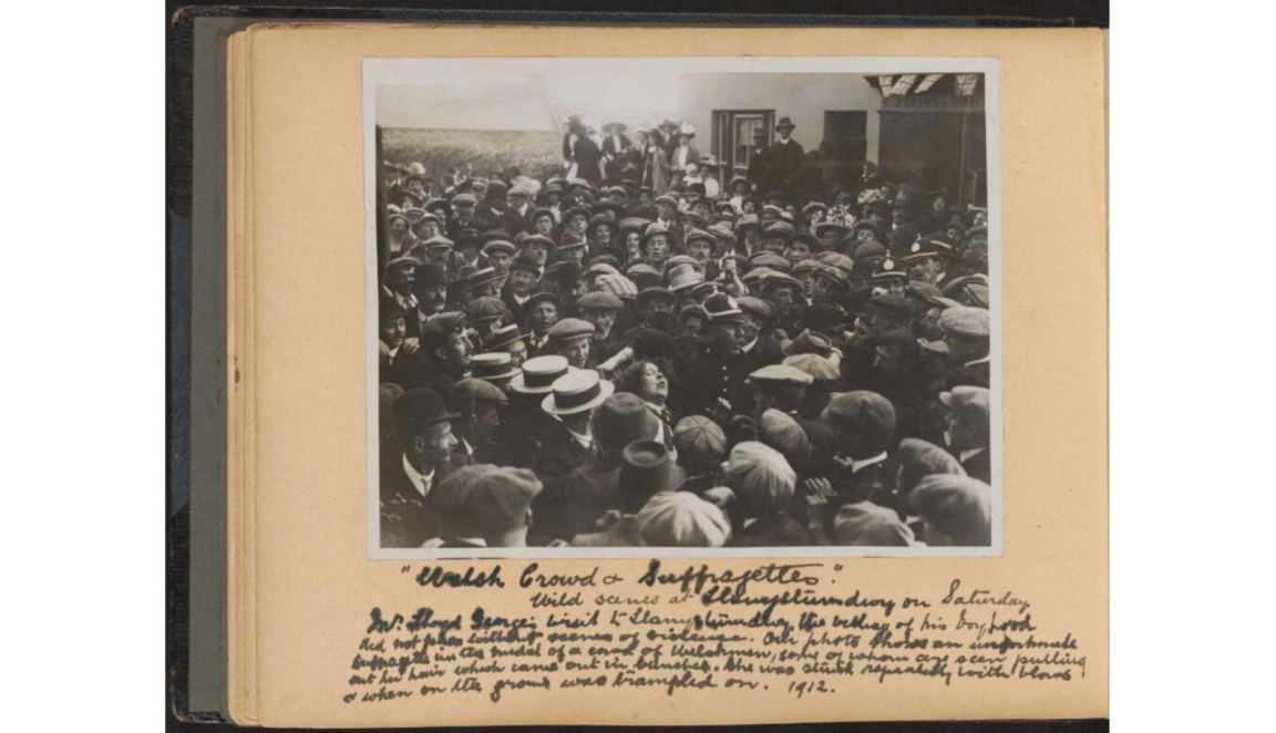 A densely packed crowd of men and women outdoors, with one woman being pulled by her hair.