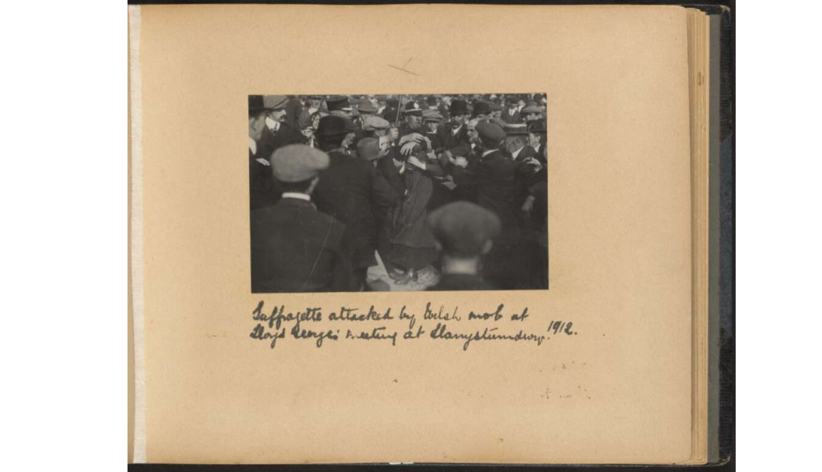 A crowd of men in hats and police officers surround a woman in dark clothing during an altercation.