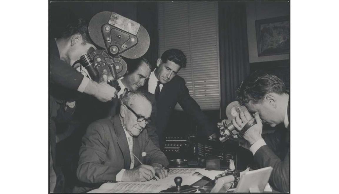 black and white photograph of man signing a contract being filmed