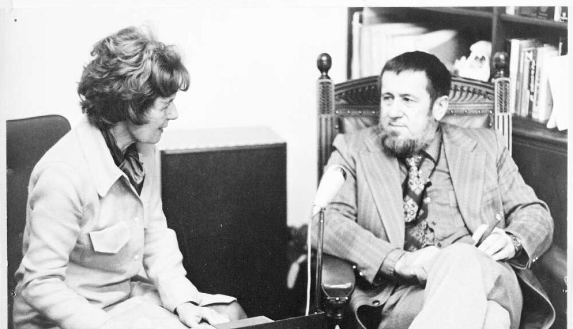 A woman sitting talking to a man while using a recorder.