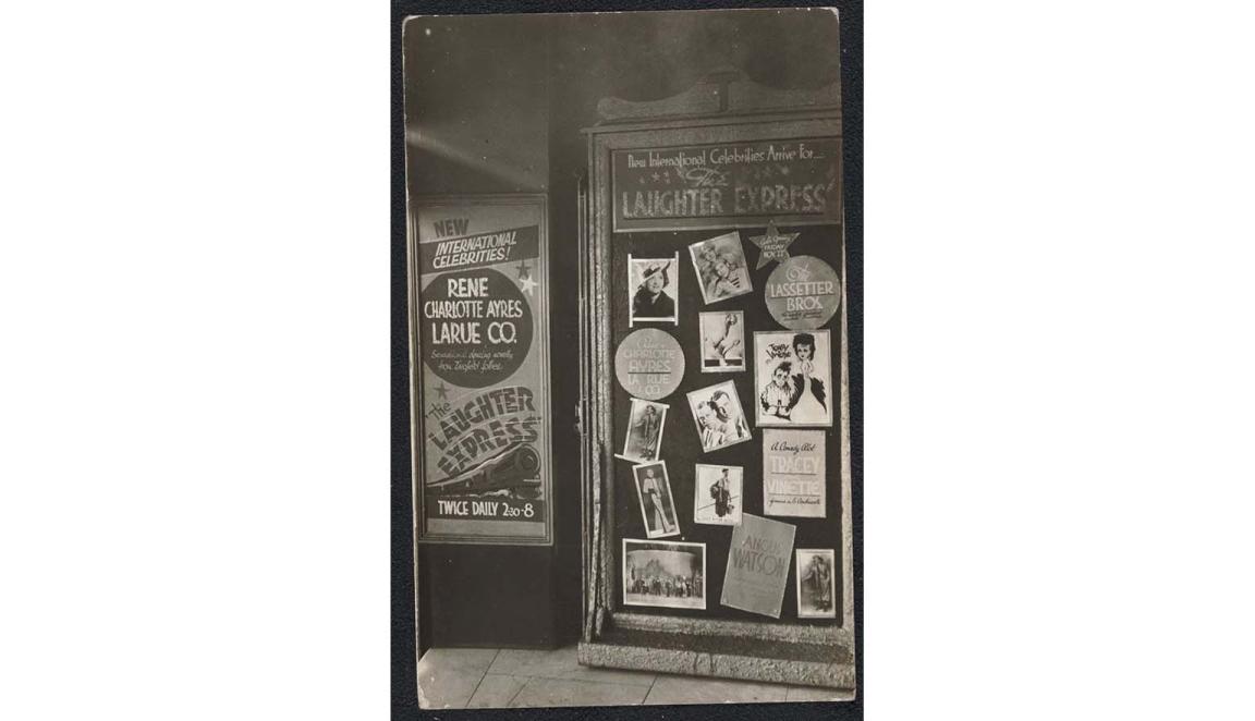 A black and white photograph of a series of billboards advertising vaudeville performances and the stars in them. One poster, for the Laughter Express, shows a steam train and the names of the performers, including Roy Rene