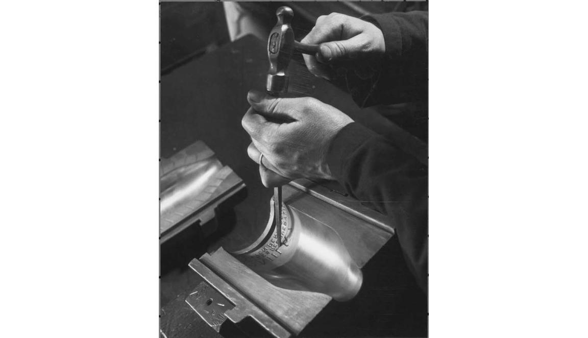 Hands engraving a milk bottle with a chisel and hammer