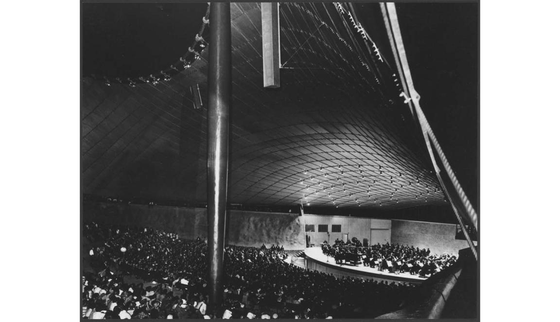 A black and white photograph of the Sidney Myer Music Bowl. A large crowd is watching a performance of an orchestra on the stage.