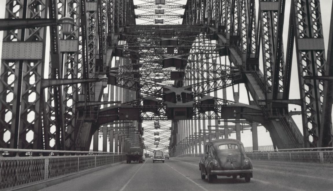 Black and white photo of cars crossing the Sydney Harbour Bridge taken from the middle of the road, 