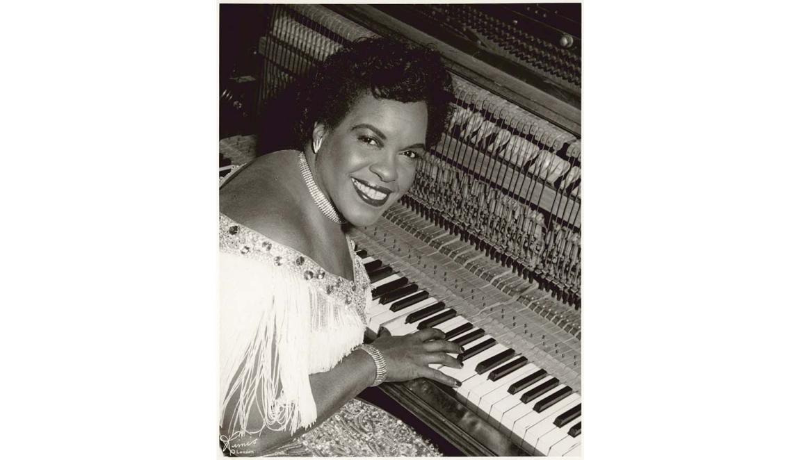 A woman sits at a keyboard and smiles at the camera.
