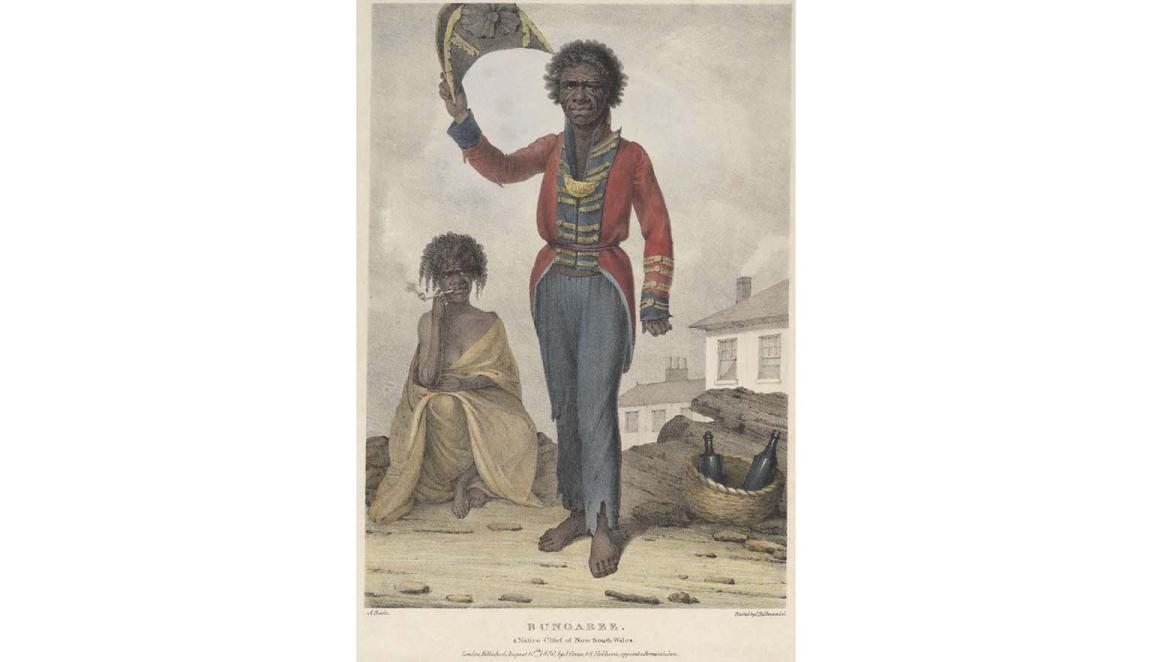 A portrait of a man. He has dark skin and hair. He is an Australian Indigenous man and is wearing a red, blue and gold European style officers coat and trousers. His trousers are tattered at the cuffs. He is holding a tricorn hat in the air. In the background an Indigenous women is seated, wrapped in a shawl. She is smoking a pipe. There is a woven basket with two empty bottles. In the background there is a white washed house with smoke curling from the chimney.