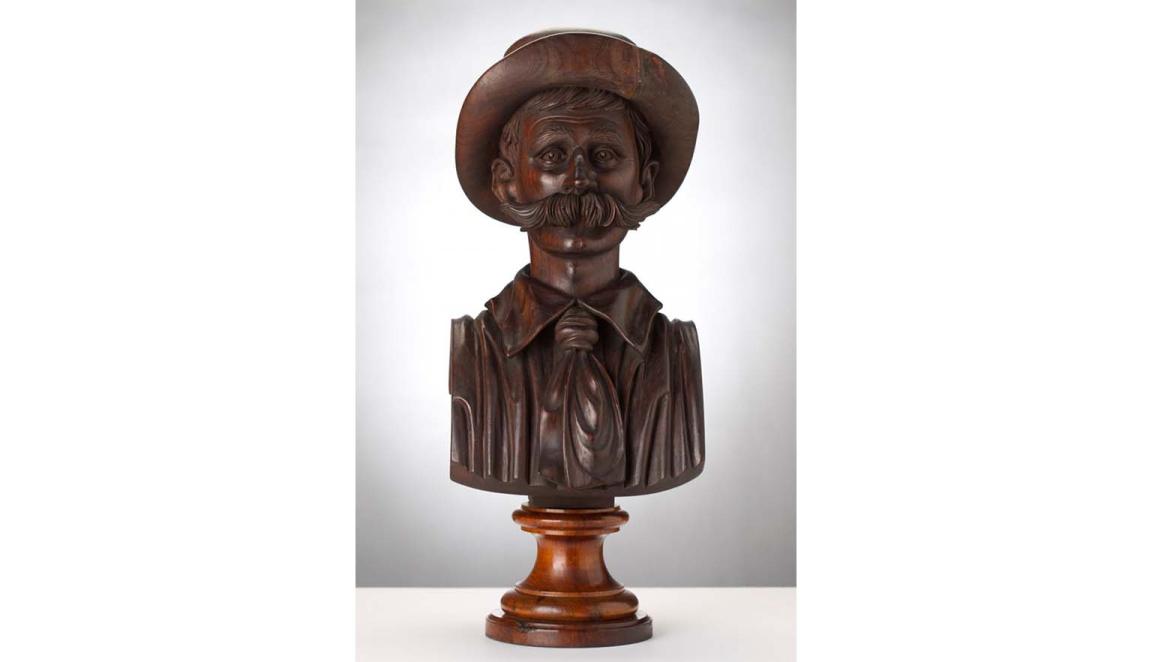 A wooden bust depicting the head and chest of Henry Lawson in a hat with large moustache.