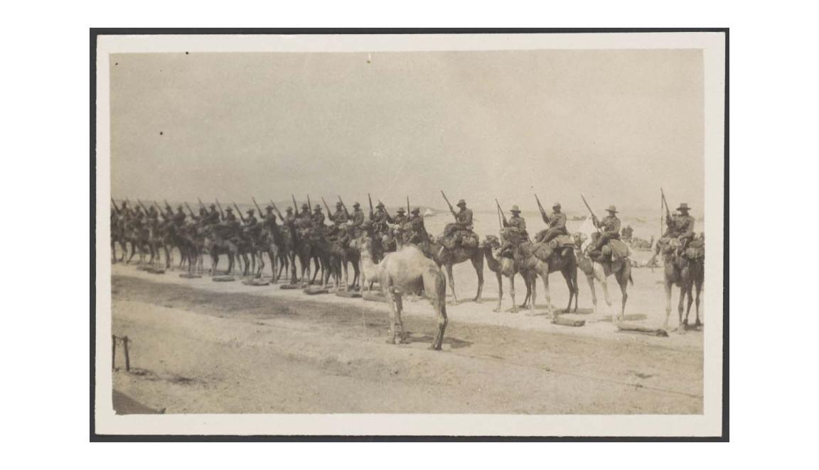 Sepia photograph of World War One soldiers mounted on camels lined up for inspection on the sand