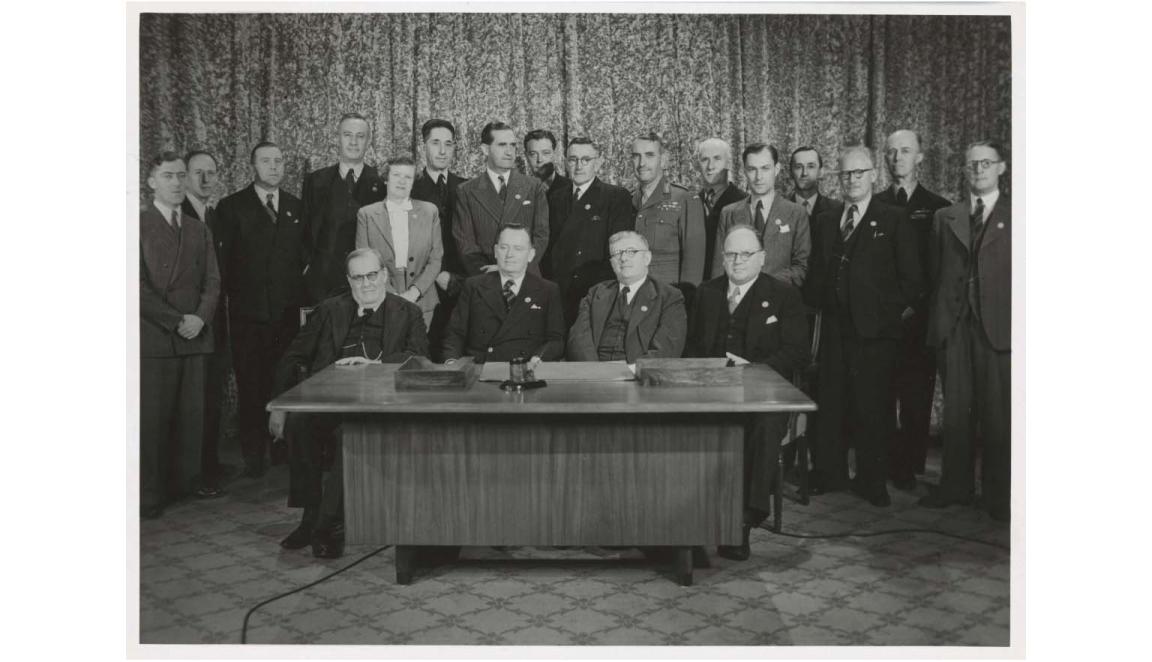 black and white photograph of a group of men gathered around a desk