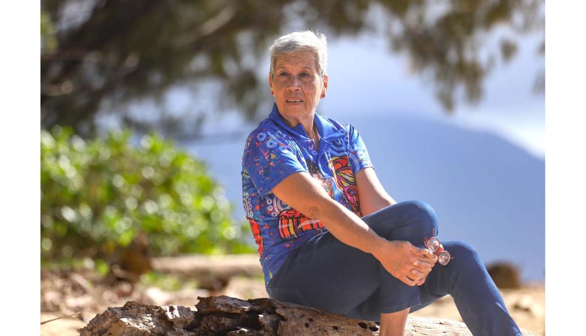 Fijian Australian woman with short grey hair sitting on a rock on a beach