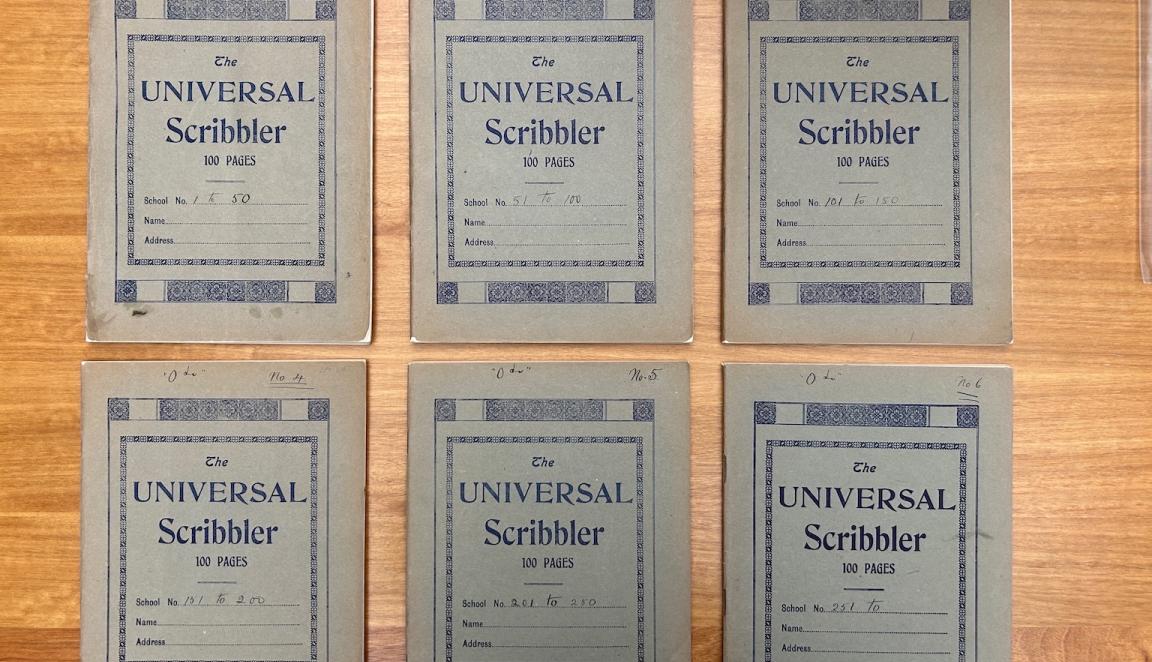 Six matching notebooks lined up, with three on the top row and three on the bottom, sitting on a wooden desk