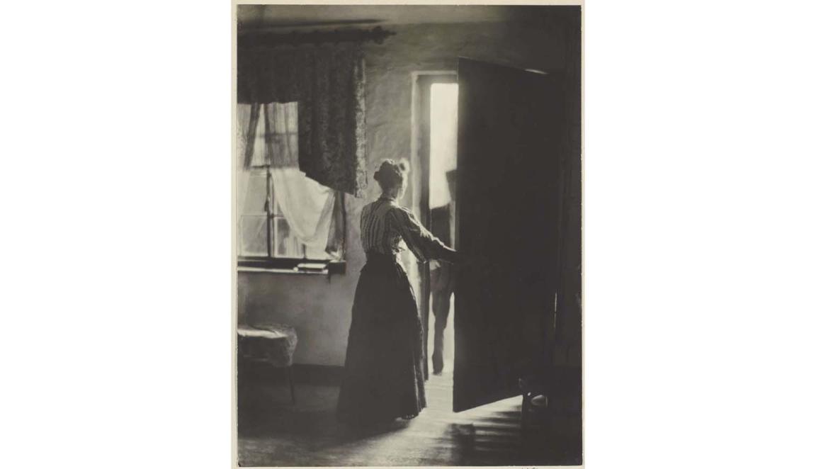 Black and white photo of a woman opening a door to a man standing on the outside of the house