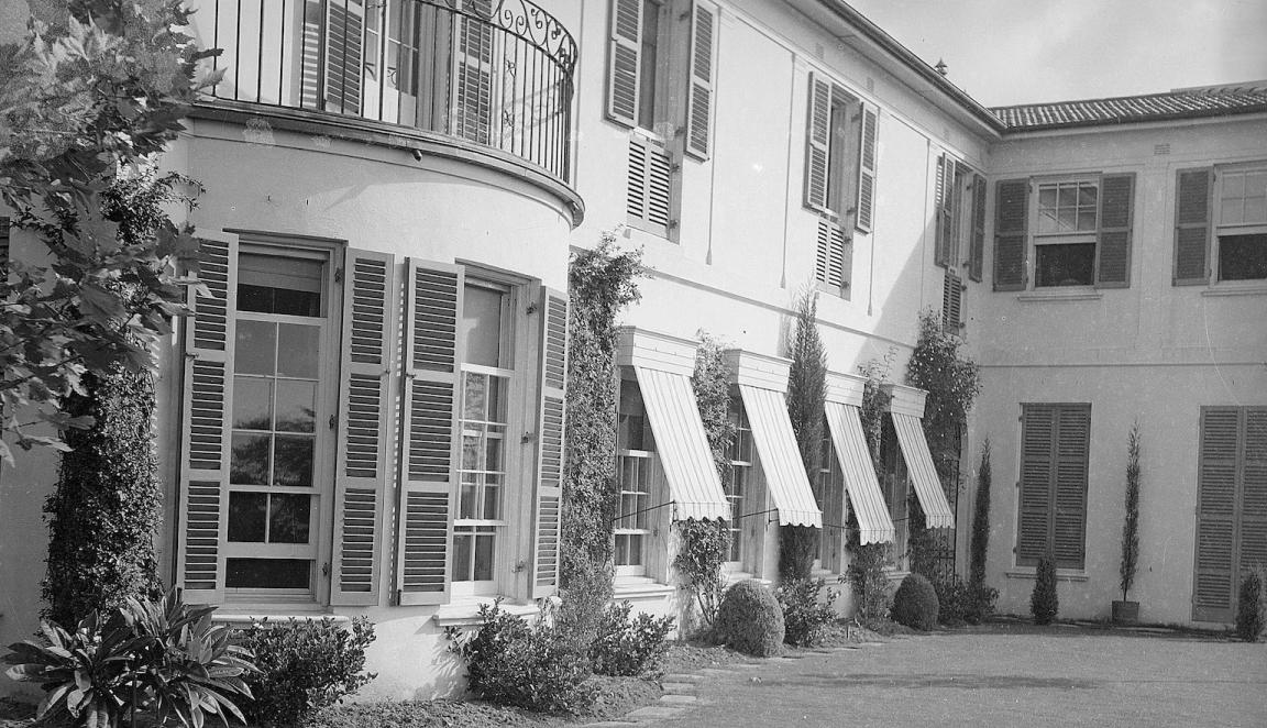Black and white photo of a nice two-storey home with lots of shutters and awnings on the windows